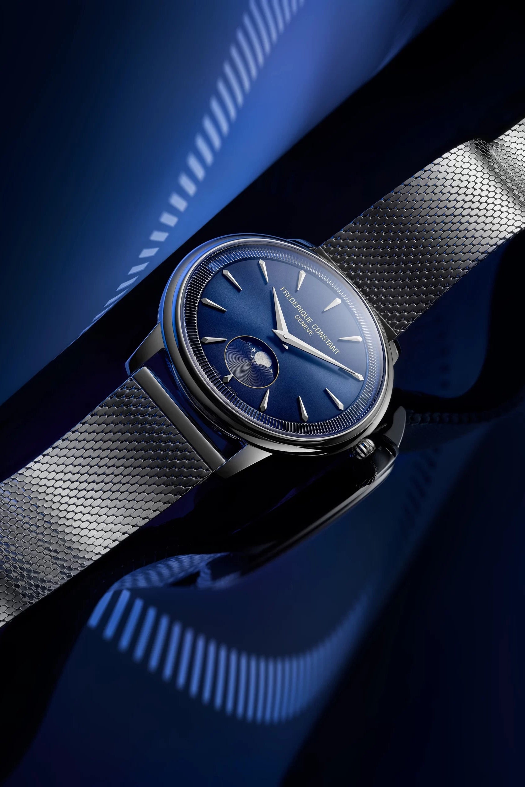 A close-up of a wristwatch with a dark blue dial, silver-toned case, and matching blue strap, photographed against a dark blue abstract background.